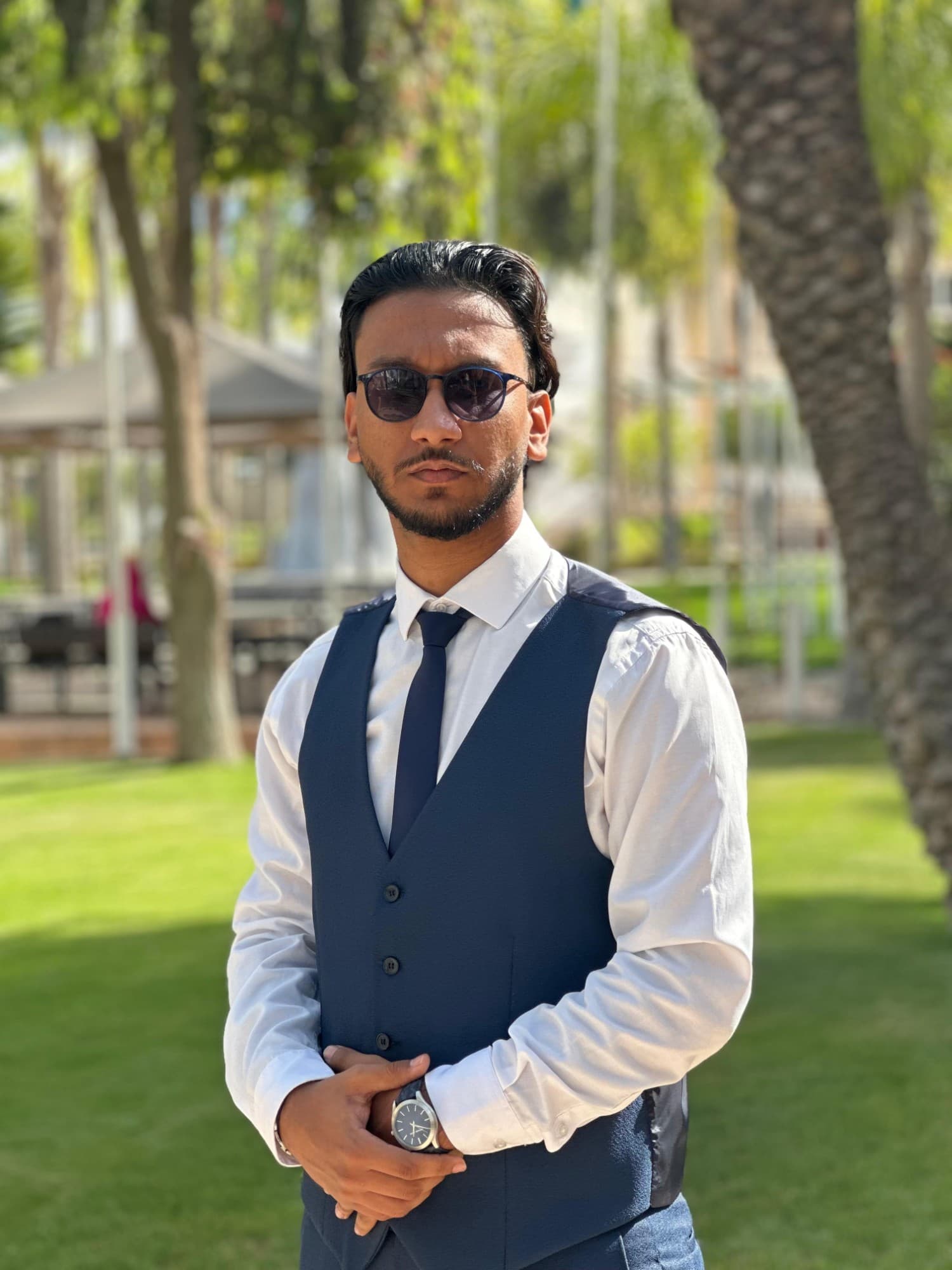 Abdellah Kachani in a navy waistcoat and tie, standing among palm trees in Agadir